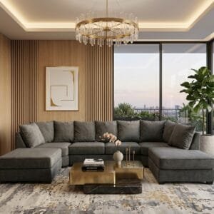 A large U-shaped charcoal grey sectional sofa with double chaises sits on a grey and gold abstract rug facing a gold tiered coffee table under a crystal chandelier.